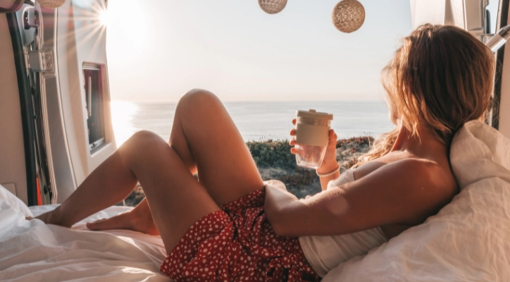 A lady enjoying a cup of tea early in the morning while looking out at the ocean.