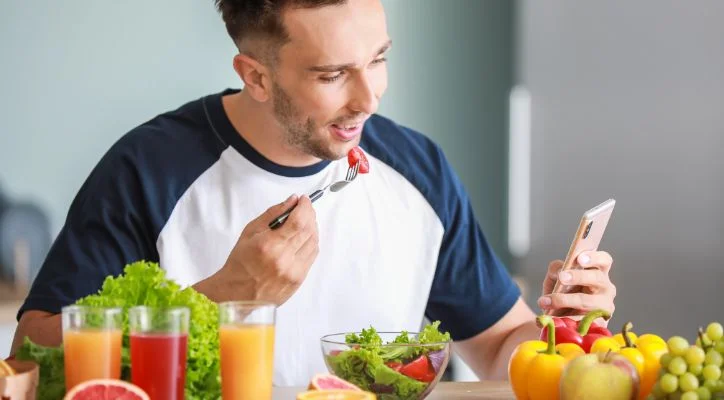 man eating vegetables and checking the calories on his cellphone